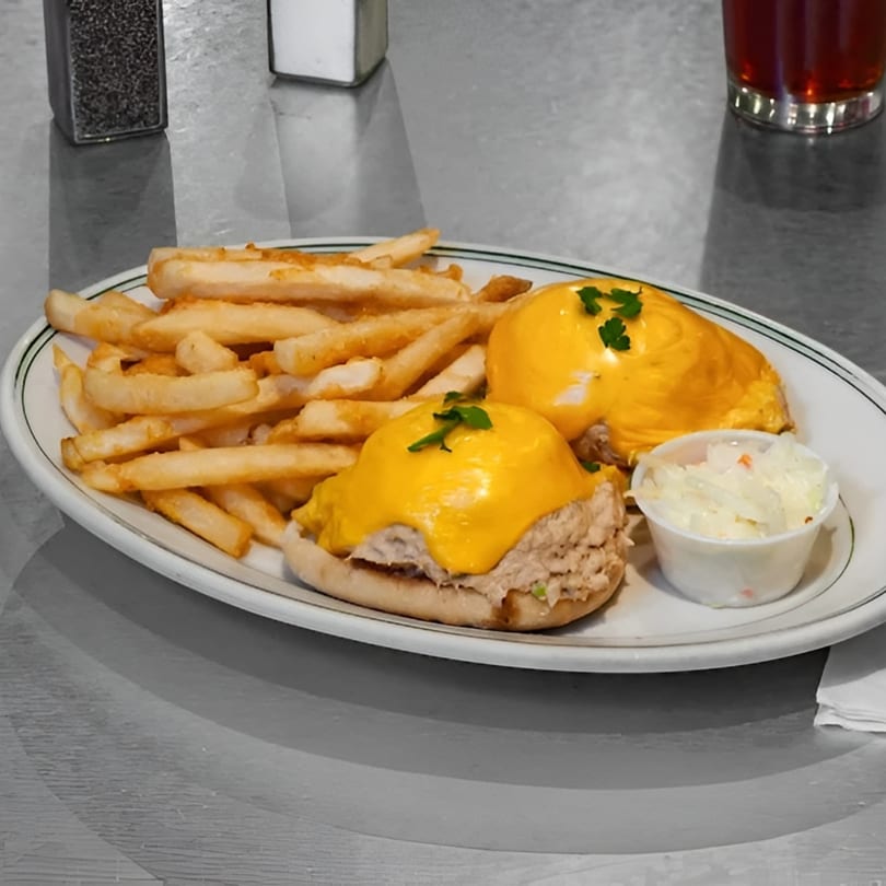 Tuna melt with melted cheese on bagels, served with french fries and coleslaw on a white plate.