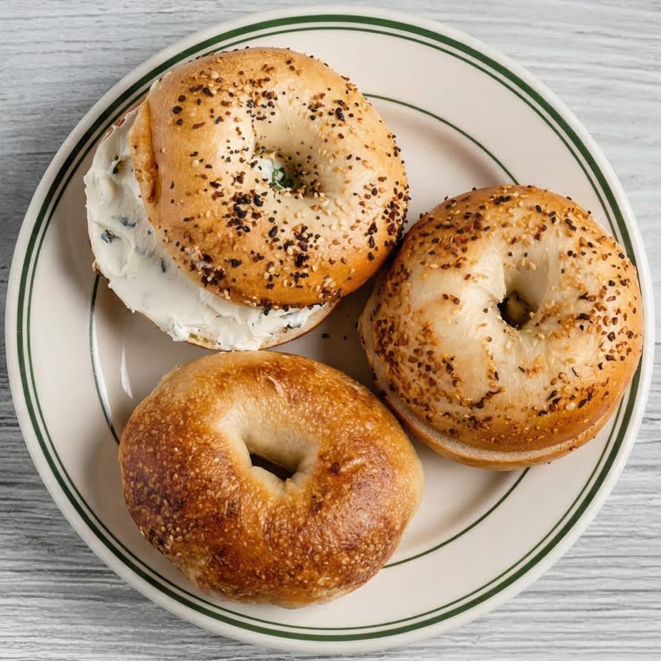 Three bagels on a white plate with green stripes, one with cream cheese and everything seasoning.