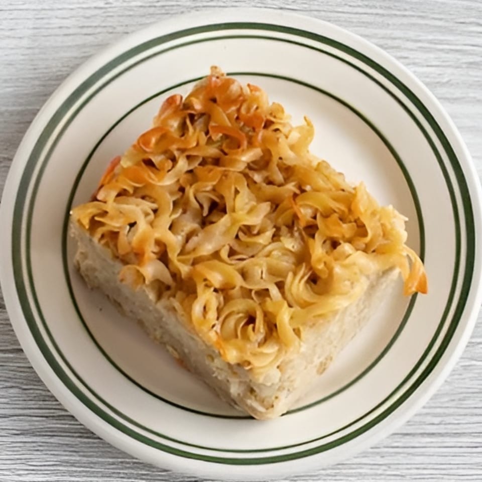 A square slice of kugel, a Jewish noodle casserole, on a white plate with green stripes.