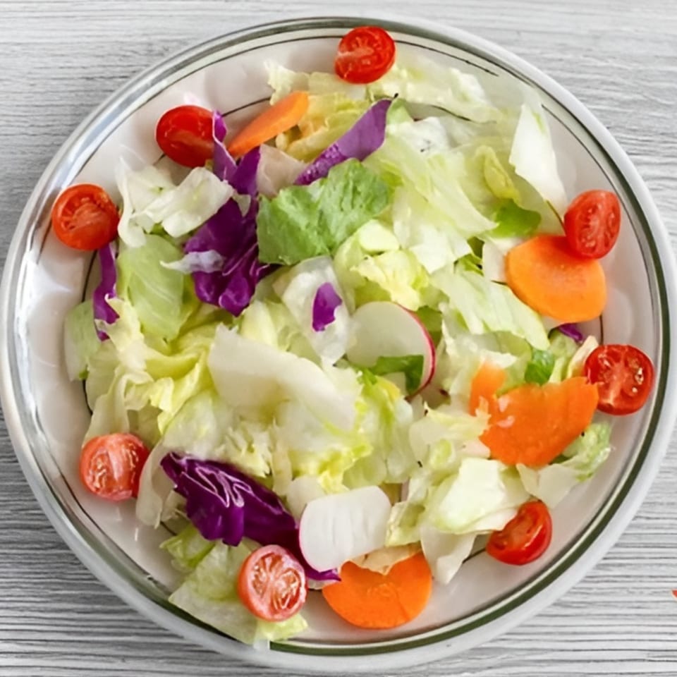 A fresh side salad with lettuce, red cabbage, carrots, radishes, and cherry tomatoes in a white bowl.